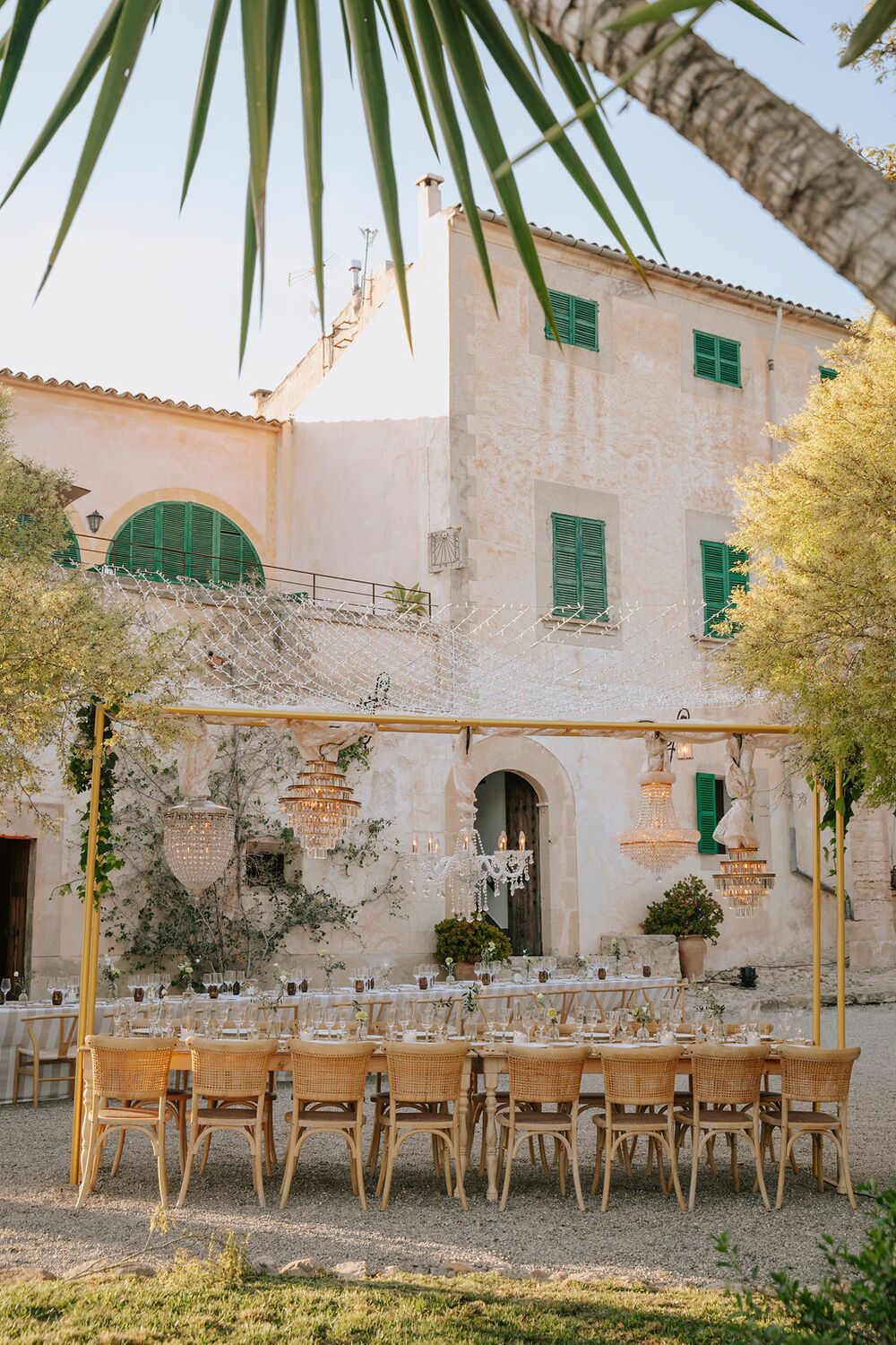 The manor façade with green shutters and a long table laid in the courtyard under golden light