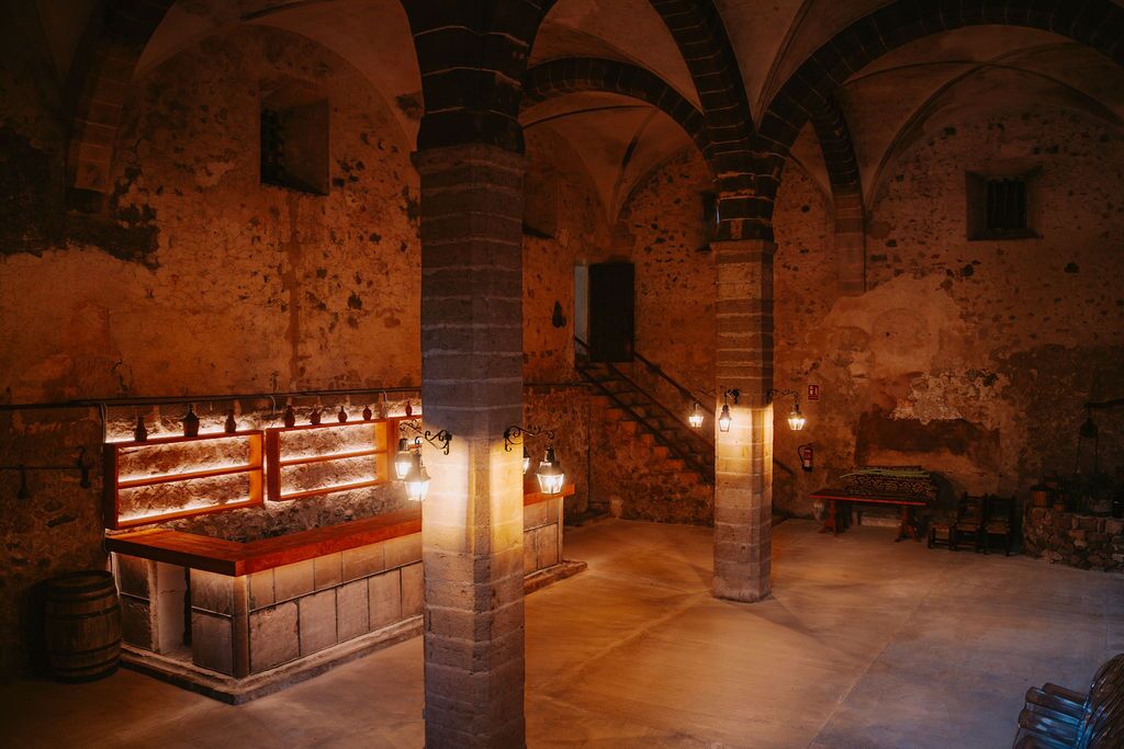 The vaulted seventeenth-century wine cellar of Son Sant Andreu, warm-lit stone ribs and a central stone column over a long bar