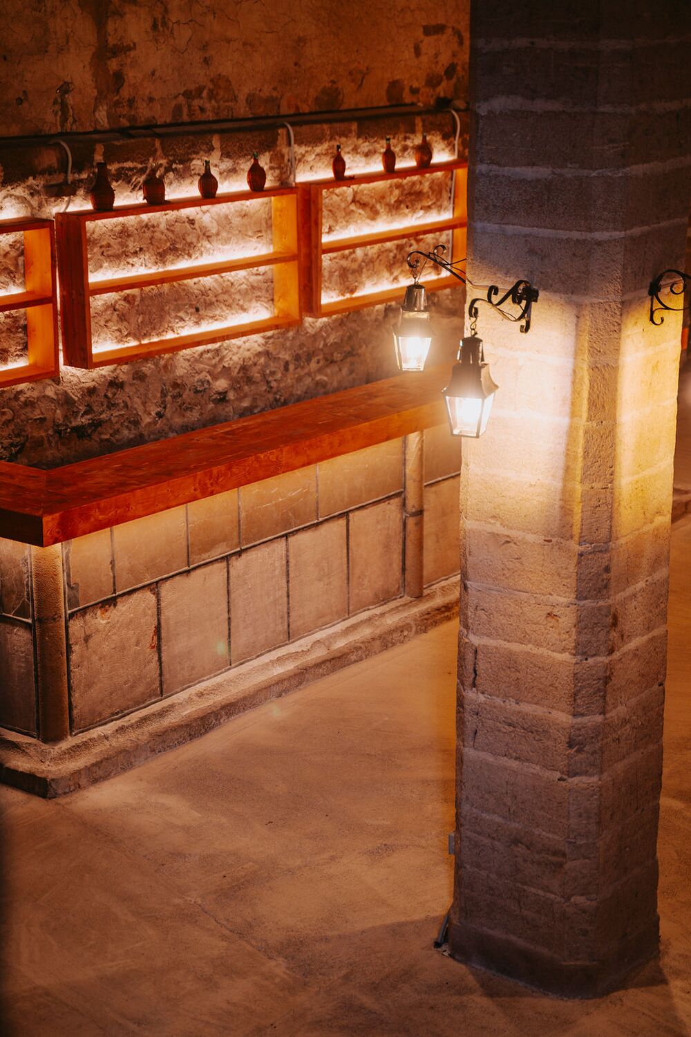 A warm-lit stone column and shelved bar inside the vaulted cellar of Son Sant Andreu