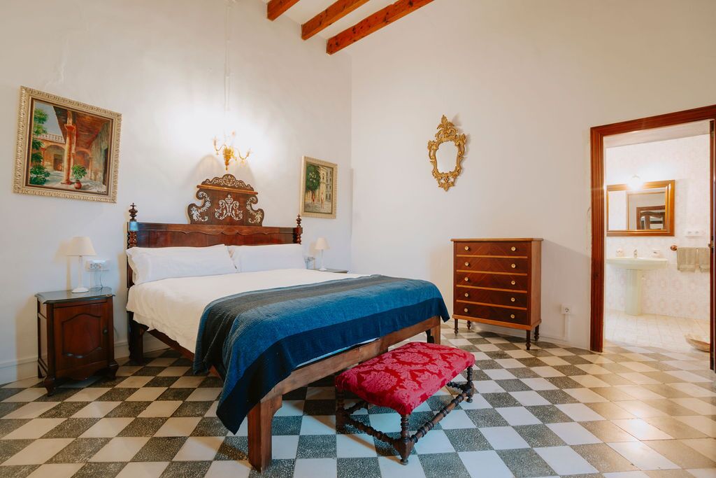 A noble-floor bedroom with a carved dark-wood headboard, blue throw, gilt mirror and a checkerboard tiled floor