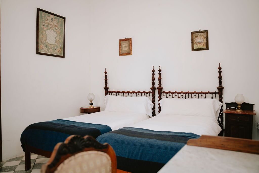 A twin room with turned-post wooden beds, blue throws, white walls and framed botanical prints