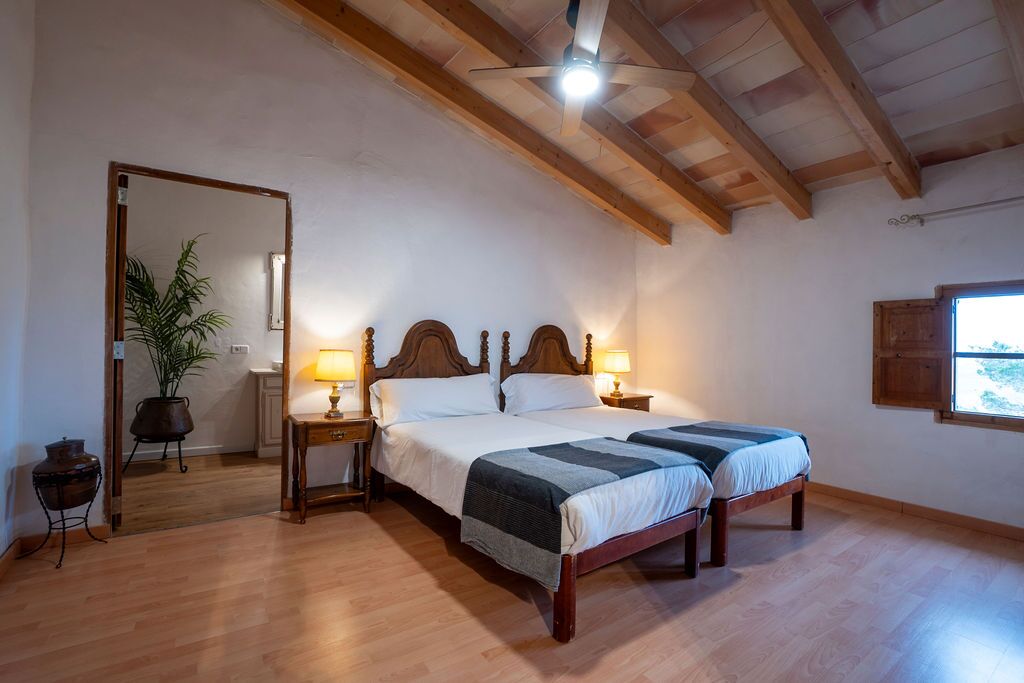 A bright upper-floor room under a beamed sloping ceiling with two beds, a tall mirror and a wooden floor