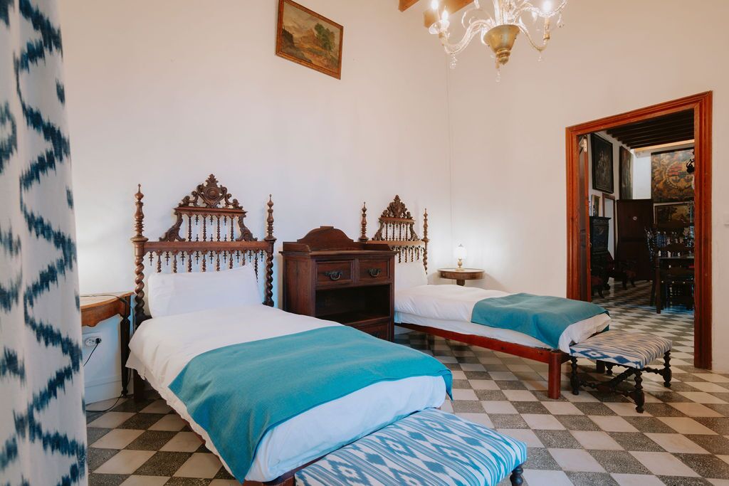 A twin bedroom with a patterned tiled floor, carved headboards and an antique writing desk