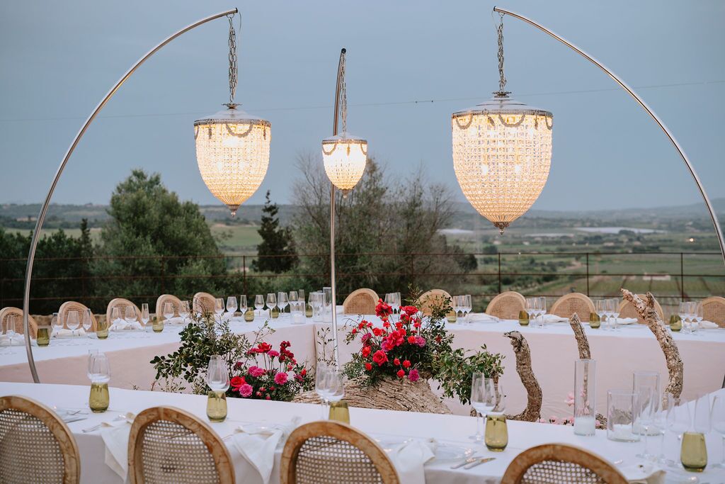 A long table set under hanging chandeliers on the terrace at dusk, the Mallorcan fields stretching out beyond