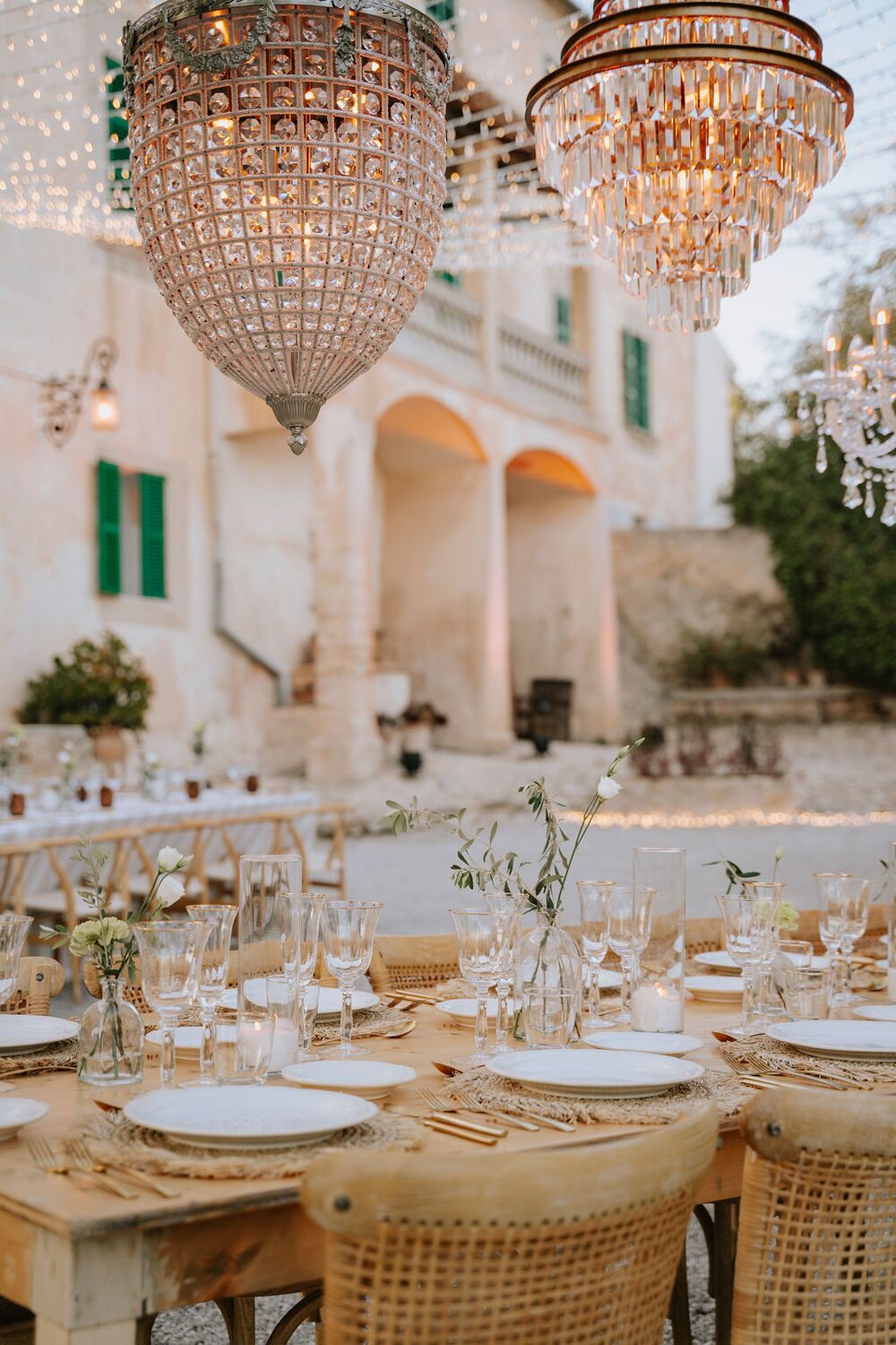 The manor façade lit with strings of festoon lights at dusk, tables set below the arches